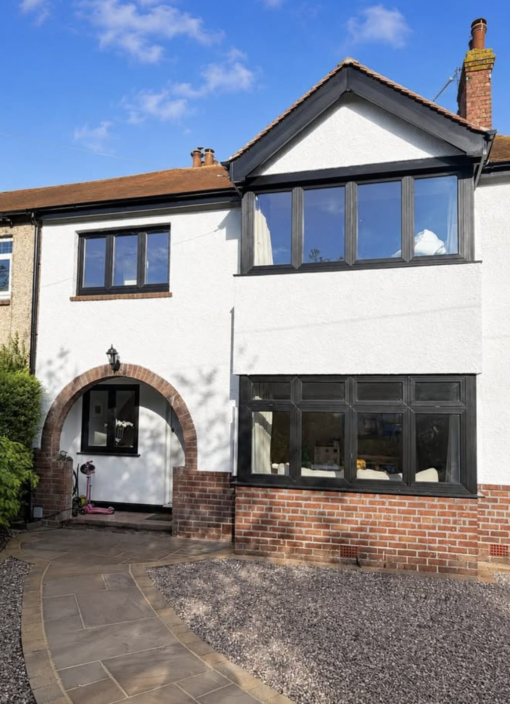 Render finished onto a retained brick plinth beneath black window frames