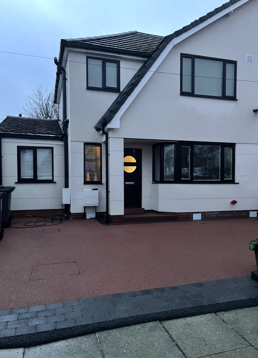 White rendered house at dusk with black window frames and a resin driveway